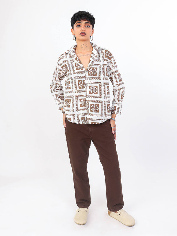 Person wearing a brown patterned shirt and brown pants on a white background