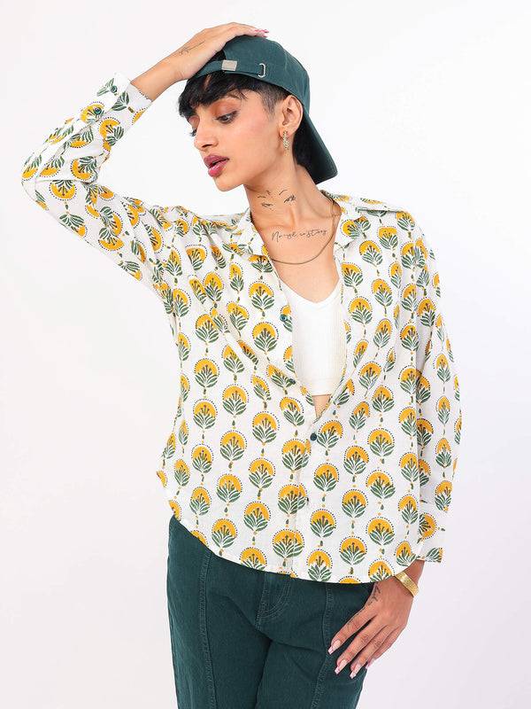 Woman wearing a Sun & Leaf shirt with green pants and cap on a white background