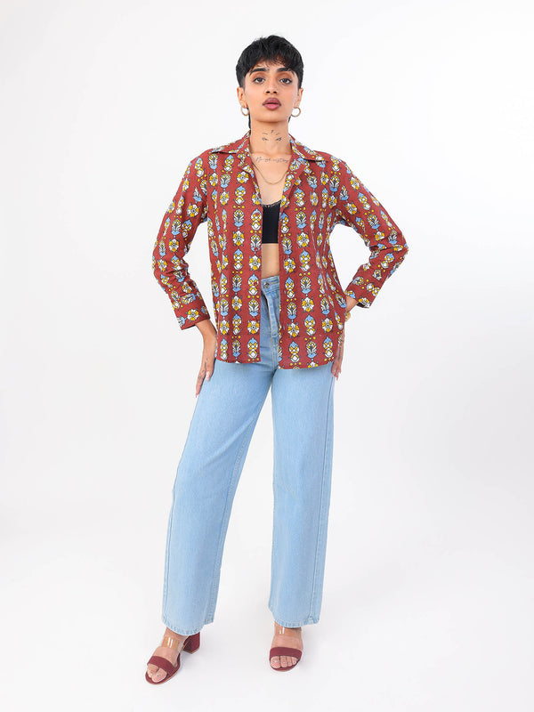 Woman wearing a patterned shirt and light blue jeans on a white background