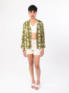 Woman wearing a green patterned shirt and white shorts on a white background