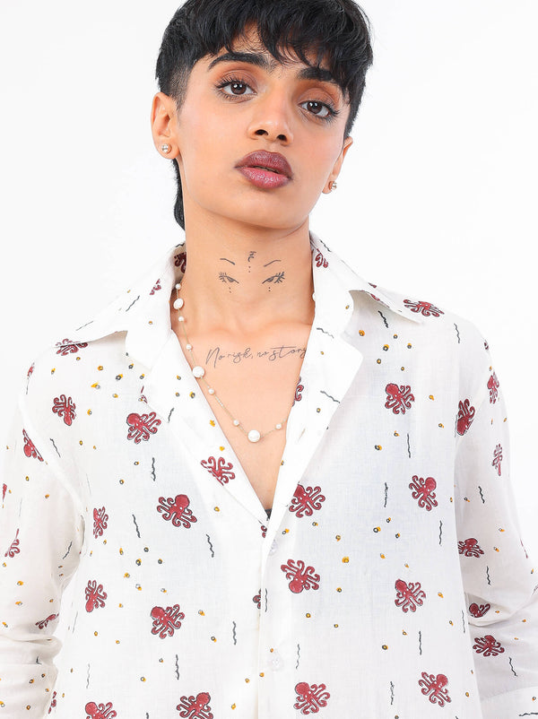 Woman wearing a white ocean print shirt andred shorts on a white background
