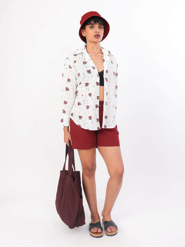 Woman wearing a white ocean print shirt andred shorts, and a red hat on a white background
